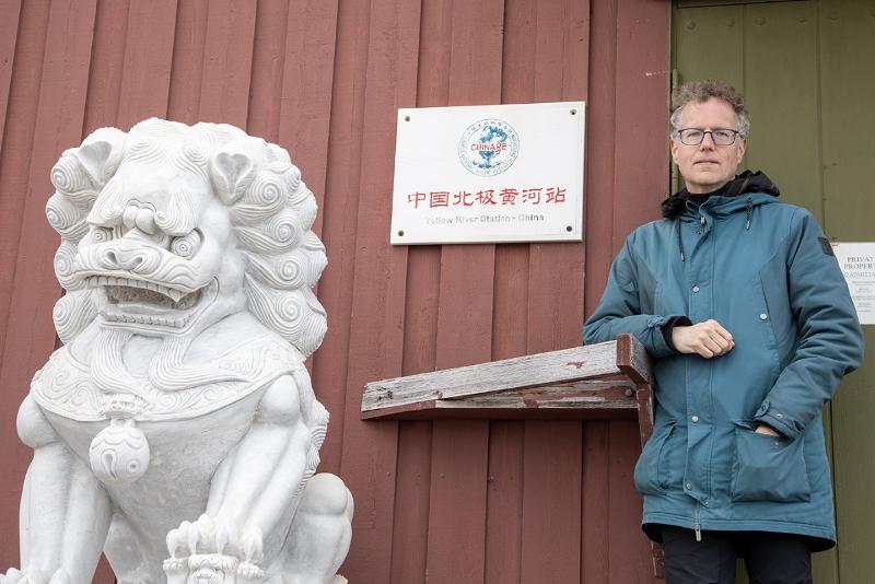 Ein mann henslengt foran ein raud bygning. Ved sidan han ein d&oslash;r, og ved sisan av den igjen ein statue av ein l&oslash;ve i kinesisk stil.